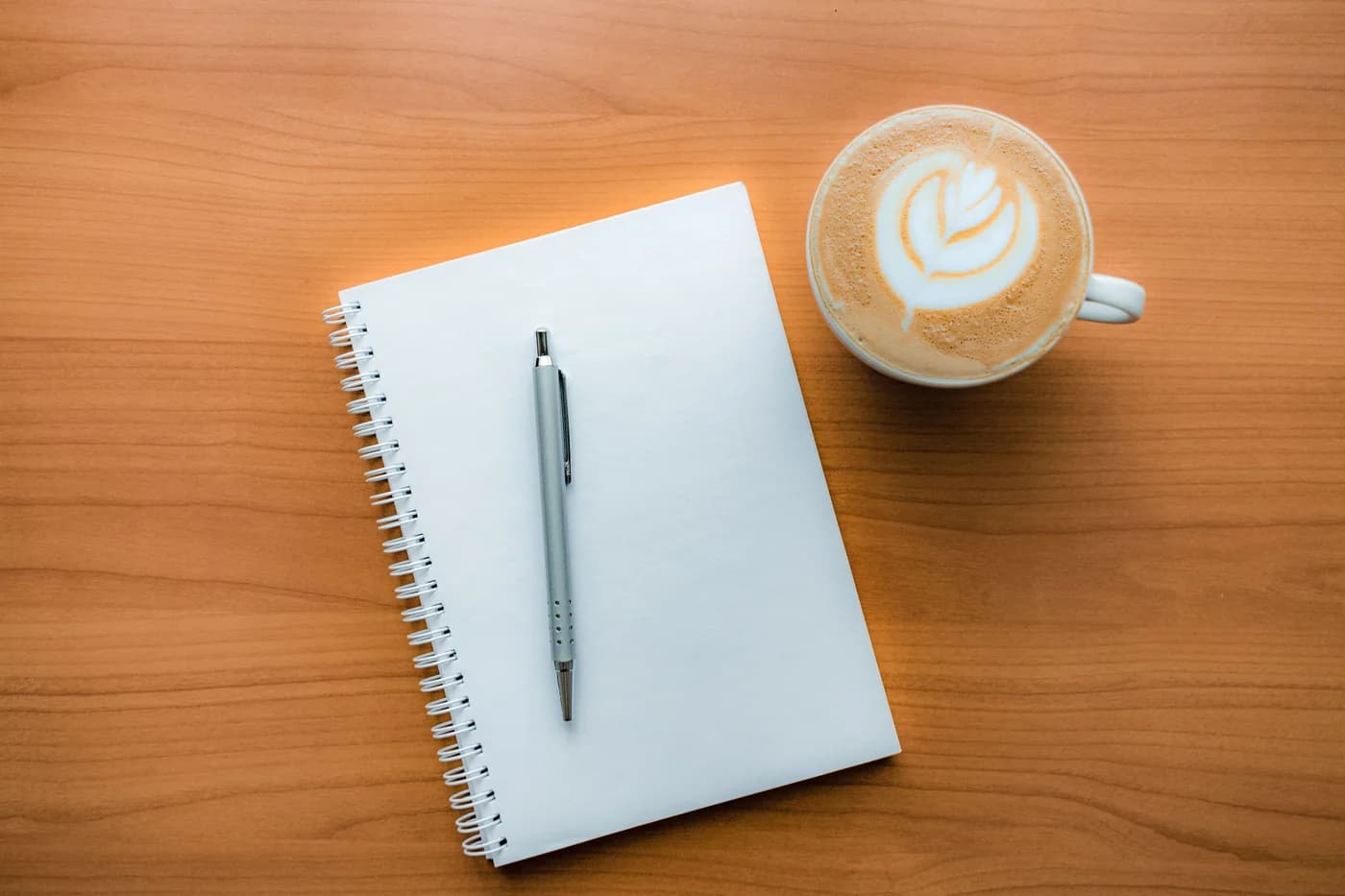 Notebook, pen, and coffee arranged on a wooden table.