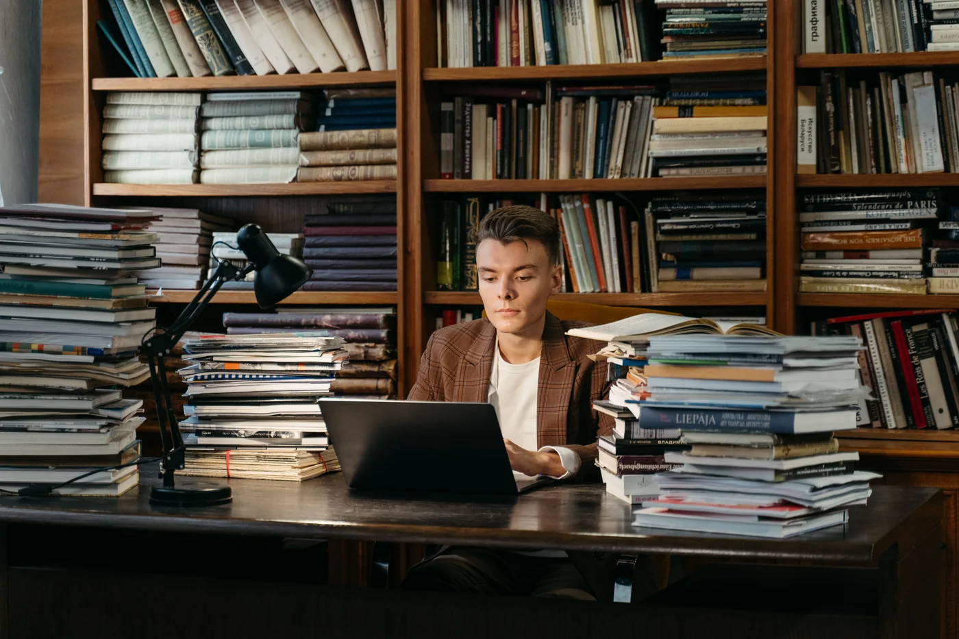 Student working on a laptop at a library desk surrounded by books.